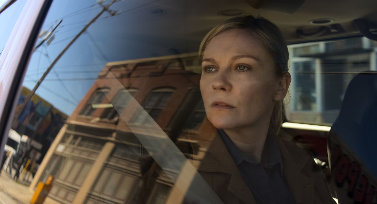 Photojournalist Lee Miller (Kirsten Dunst) sits in a car and pensively looks out of the window at the small town reflected in the glass in Alex Garland’s Civil War