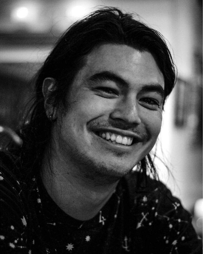 A black-and-white photo of Jason Lentz, a man with long back hair, smiling at the camera