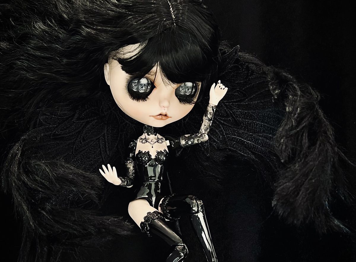 A custom Blythe tricked out with skulls for eyes, a black leather suit and boots, and giant black hair