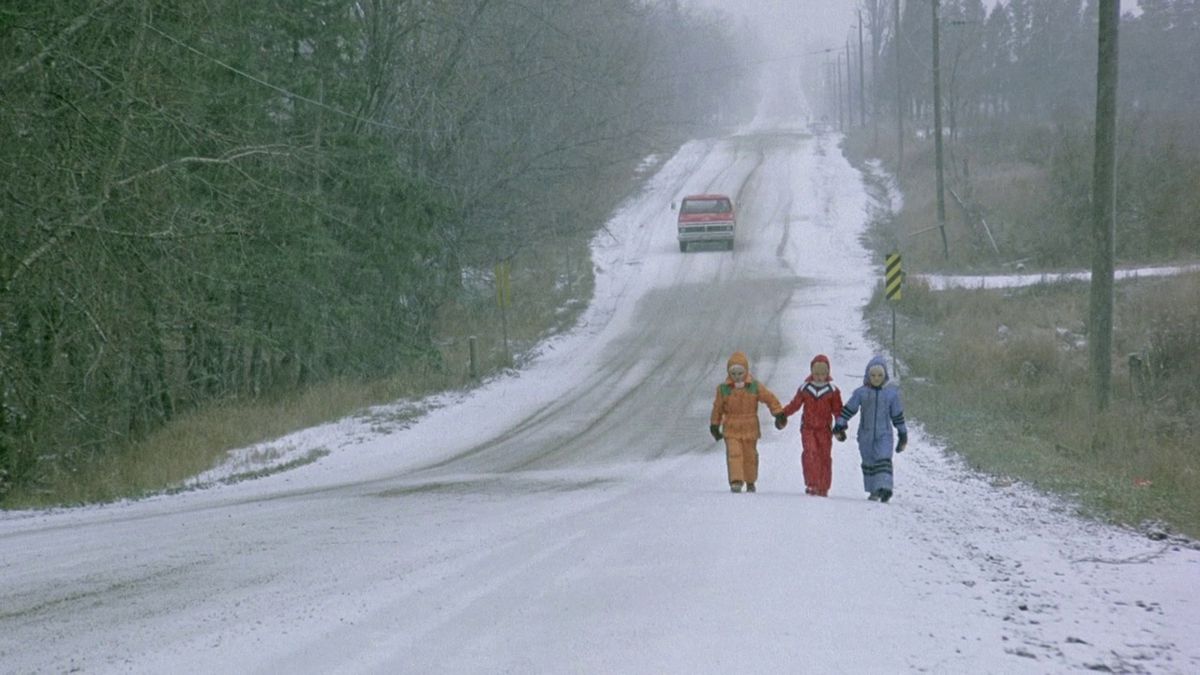 The brood from The Brood walk down a snowy street in snowsuits, holding hands.