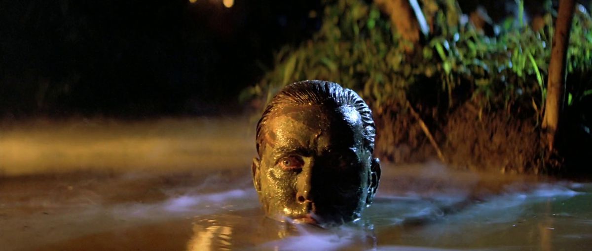 Martin Sheen as Benjamin Willard wearing face camouflage and emerging from a body of water draped in moonlit shafts of fog in Apocalypse Now.