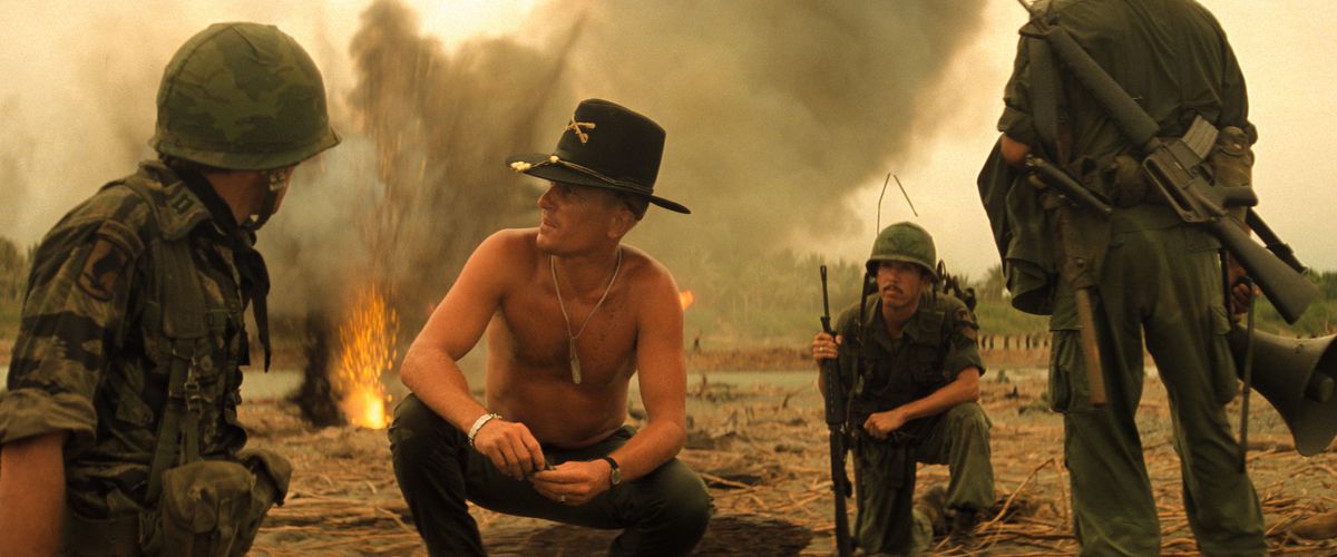 Robert Duvall crouches shirtless wearing a cowboy hat near several soldiers in Apocalypse Now