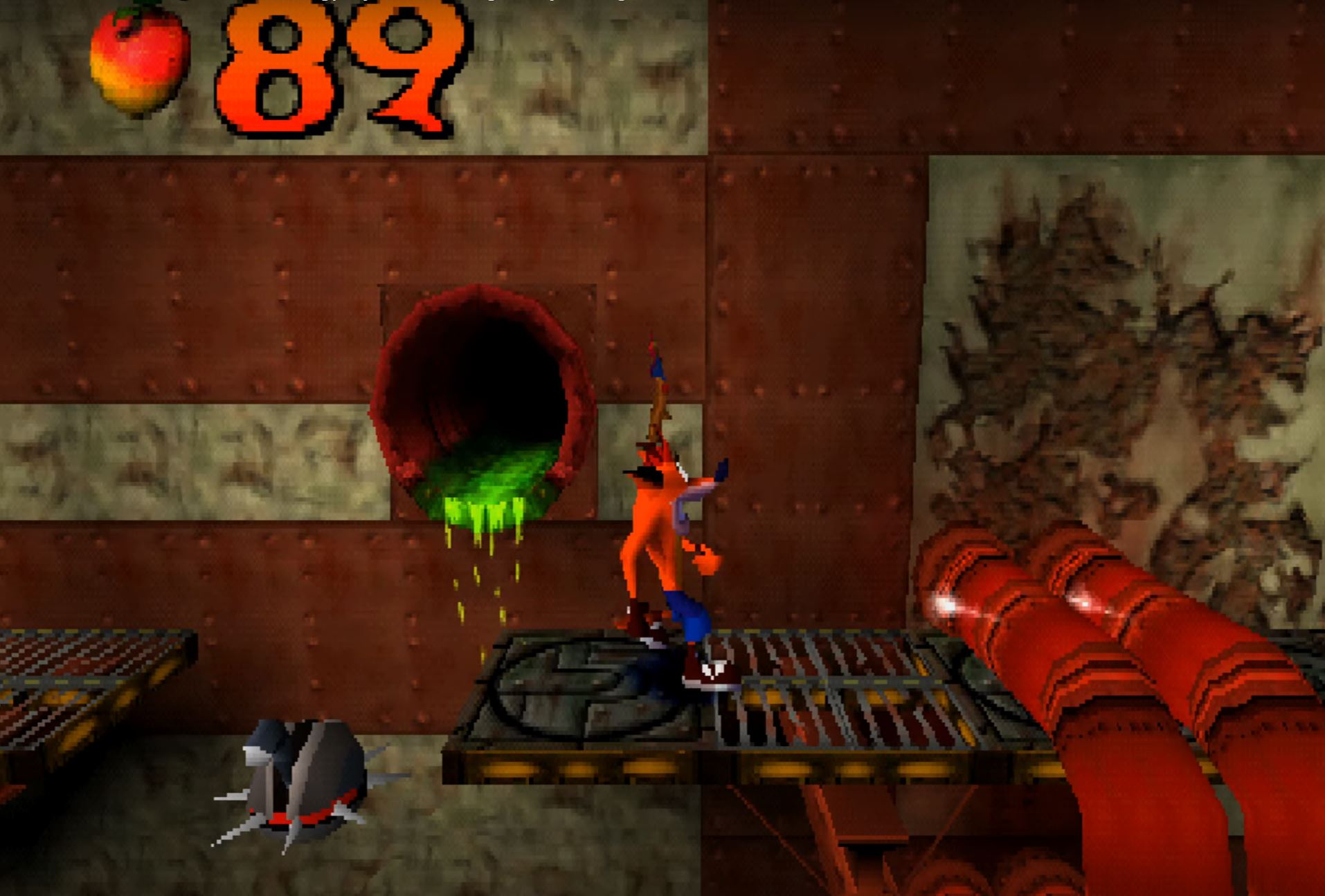 Crash Bandicoot runs across metal platforms past a culvert leaking green sludge, towards huge some orange pipes