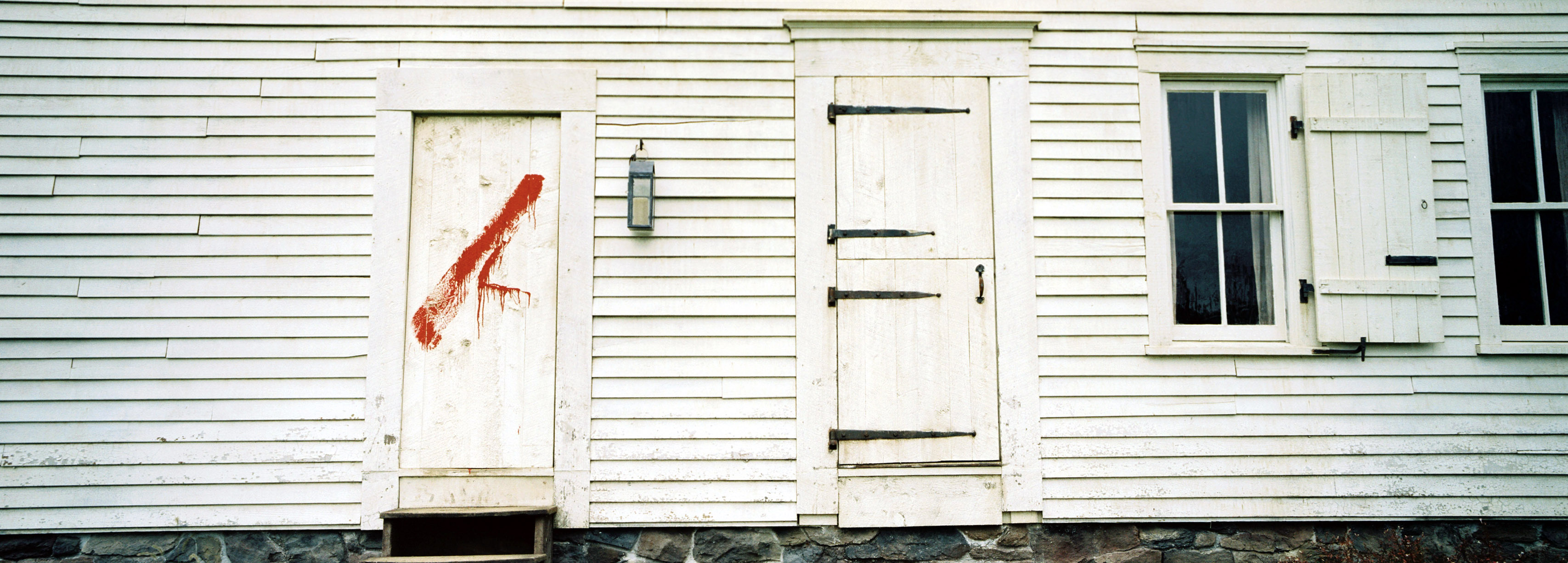 A white house with one door that has dark red blood splattered across it from The Village