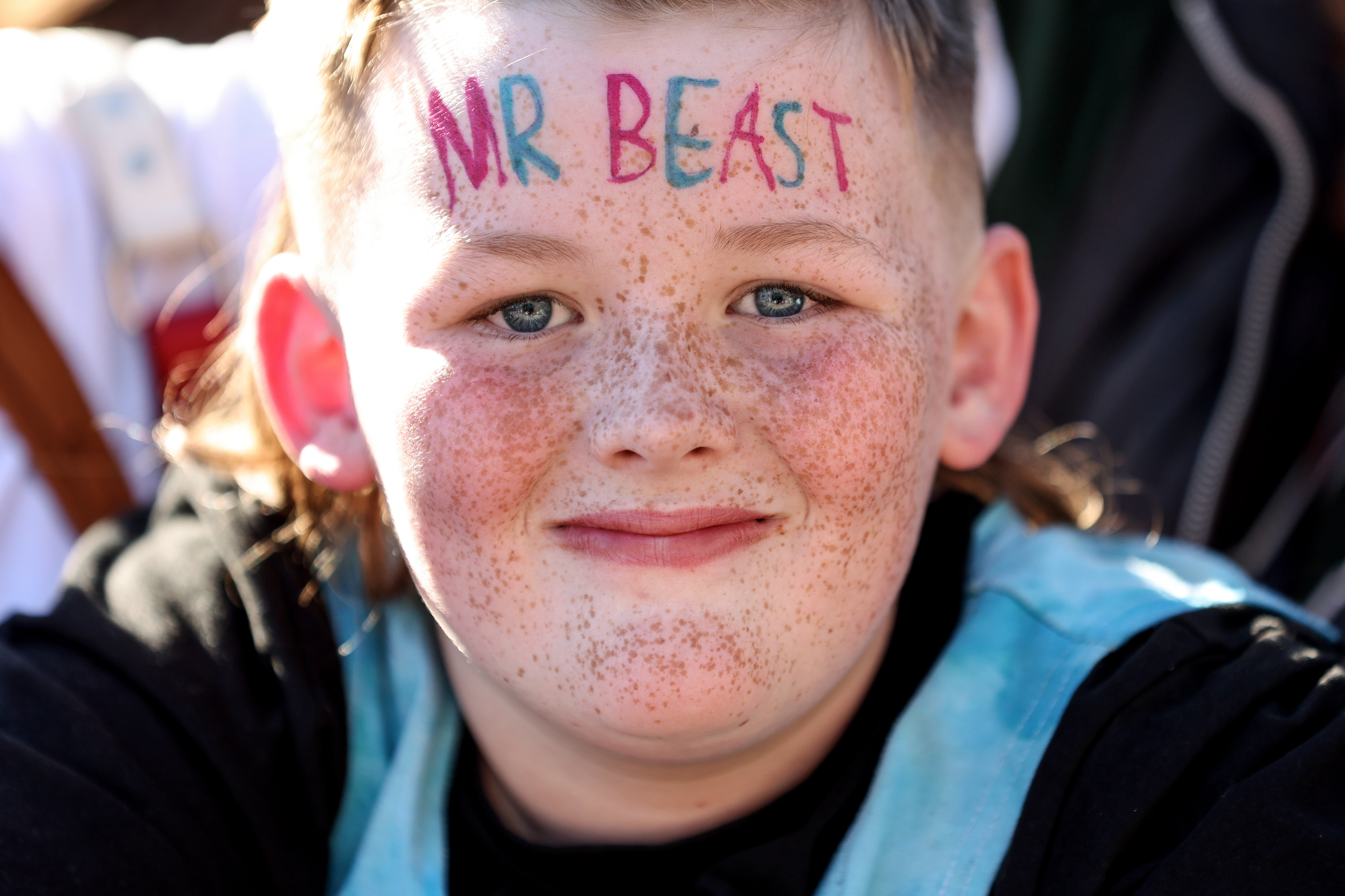 A freckled kid with MrBeast drawn on his forehead in red and green marker looks at the camera