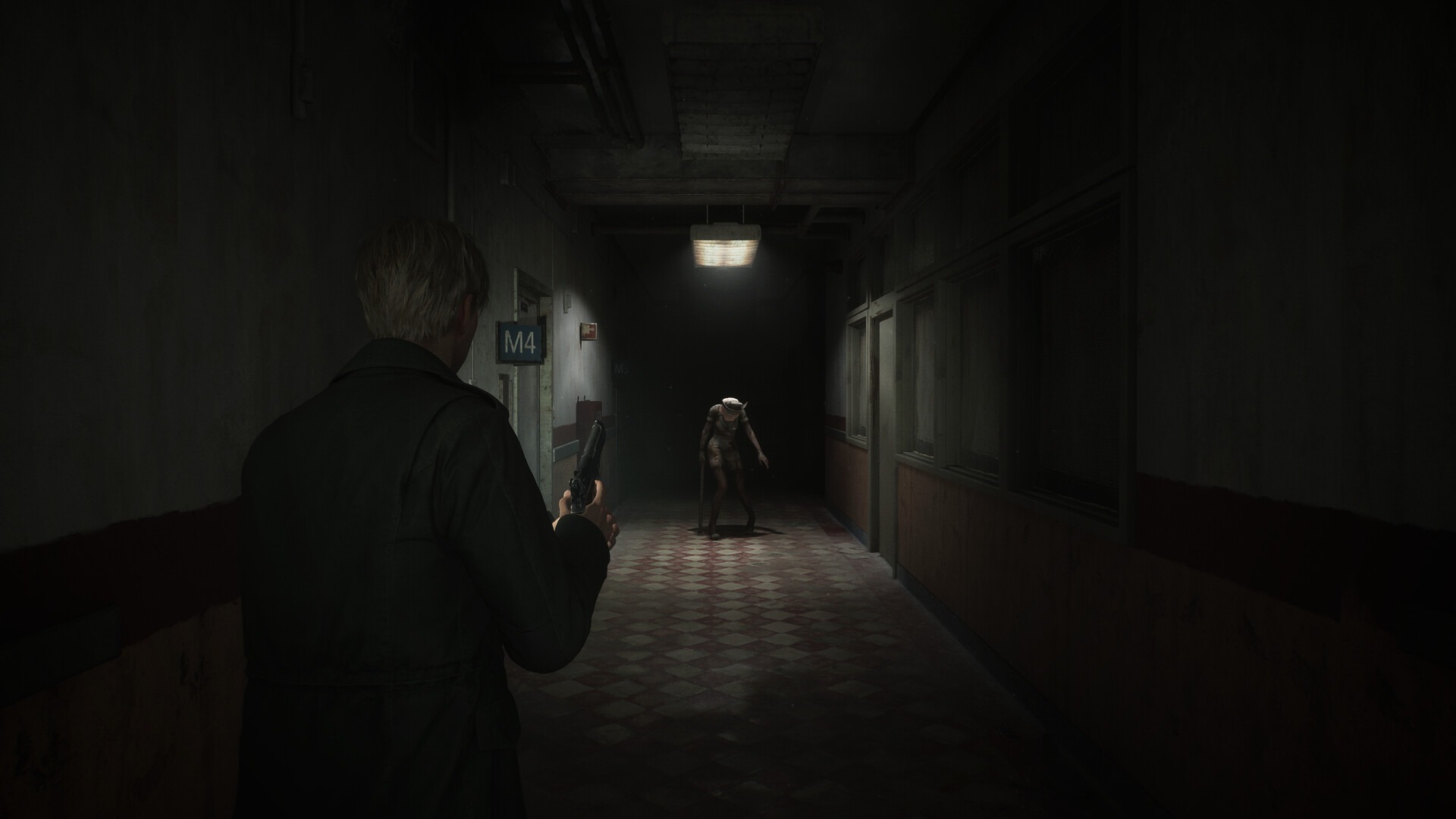 James, the protagonist of Silent Hill 2, stands in a hallway brandishing a pistol. At the end of the hallway, there’s a mannequin monster approaching him