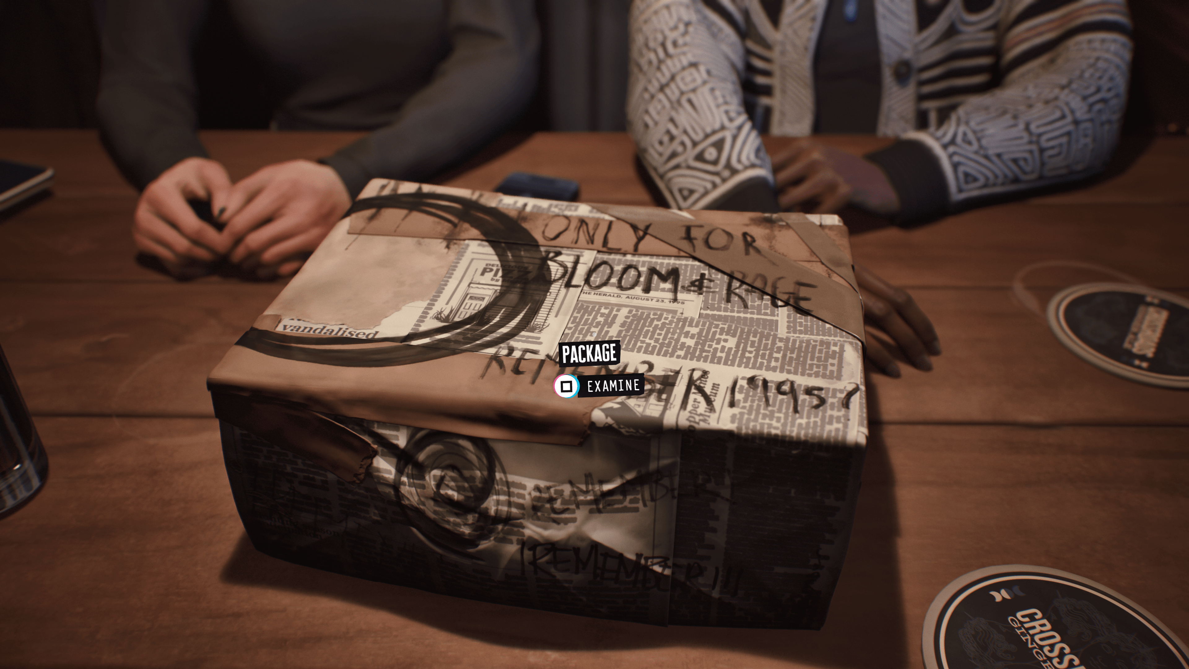 A screenshot from Lost Records: Bloom & Rage depicting a box wrapped in newspaper sitting on a table. Some other people’s hands are in the shot as well, near the box
