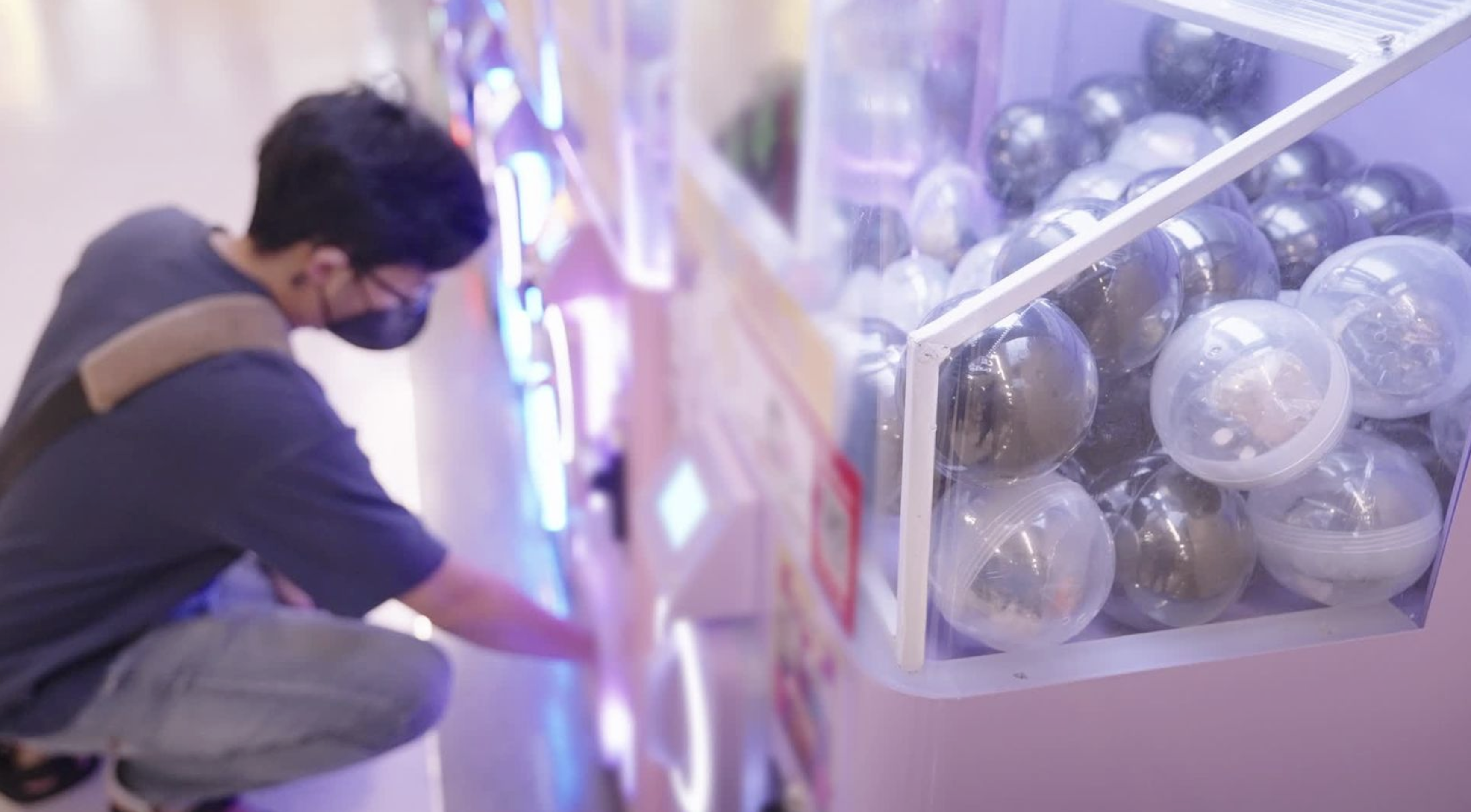 A man kneels to pull a prize out of a gacha machine.